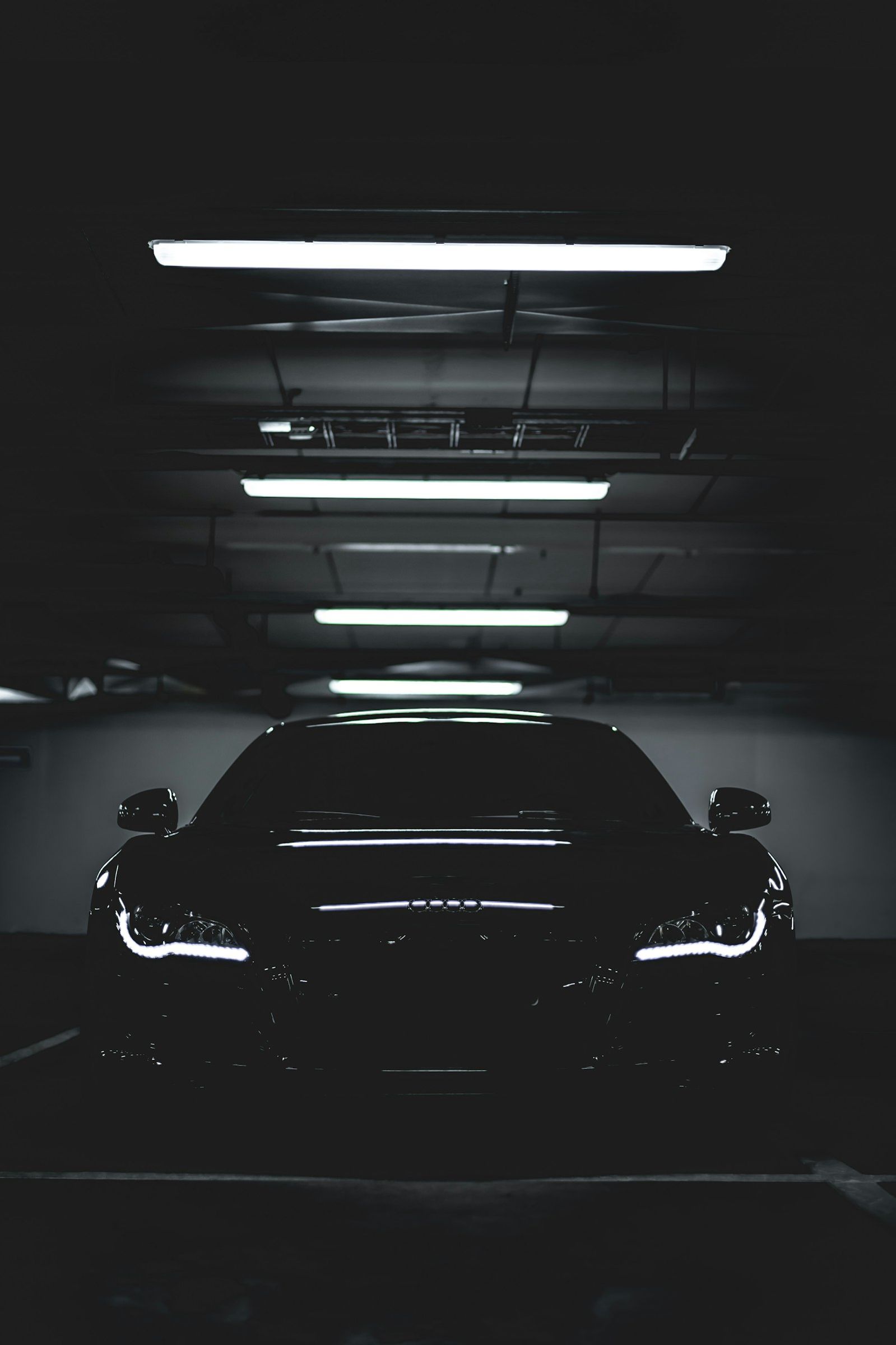 A dark sports car under strip lights in a detailing bay