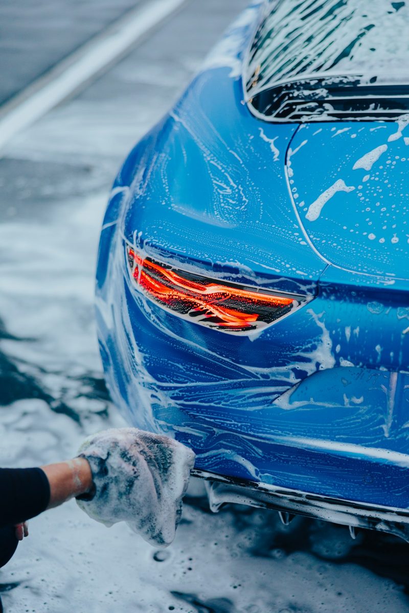 A person washing a blue car with a rag