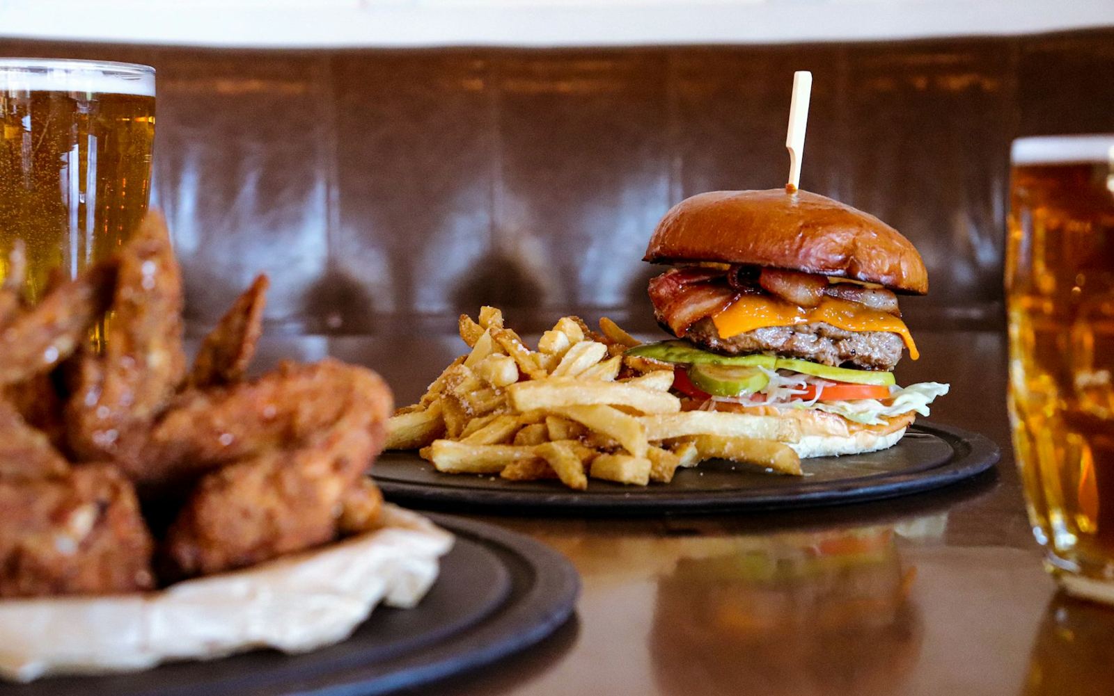 Wings and a burger on plates with beer at the bar