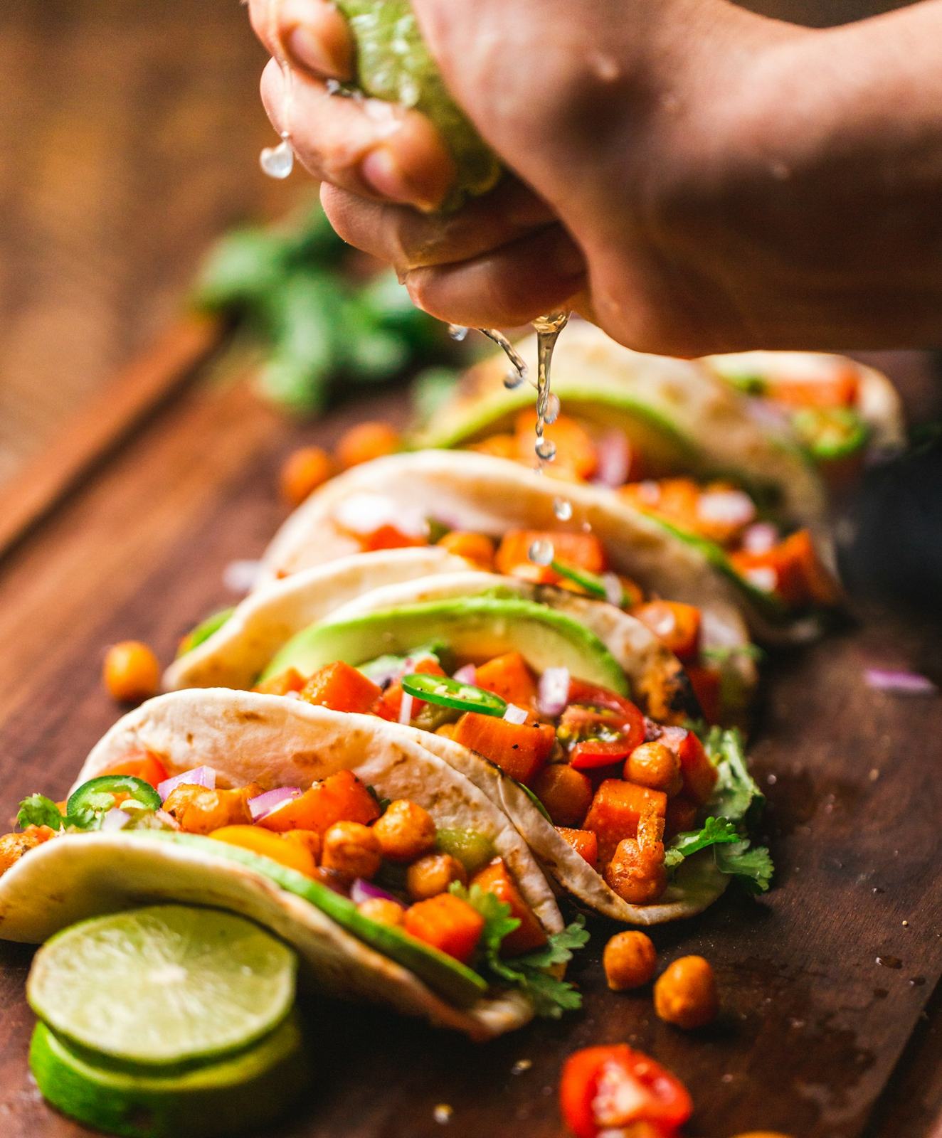A hand squeezing lime over a row of tacos
