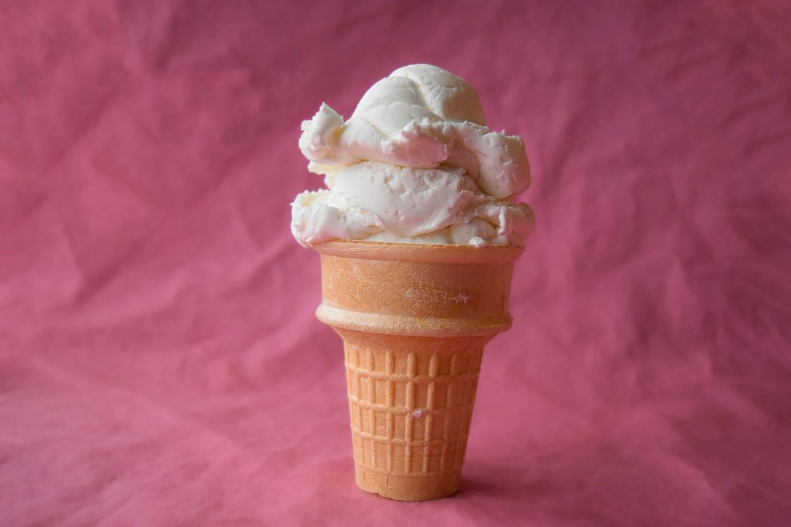 A tall scoop of cream gelato in a cone on a pink background