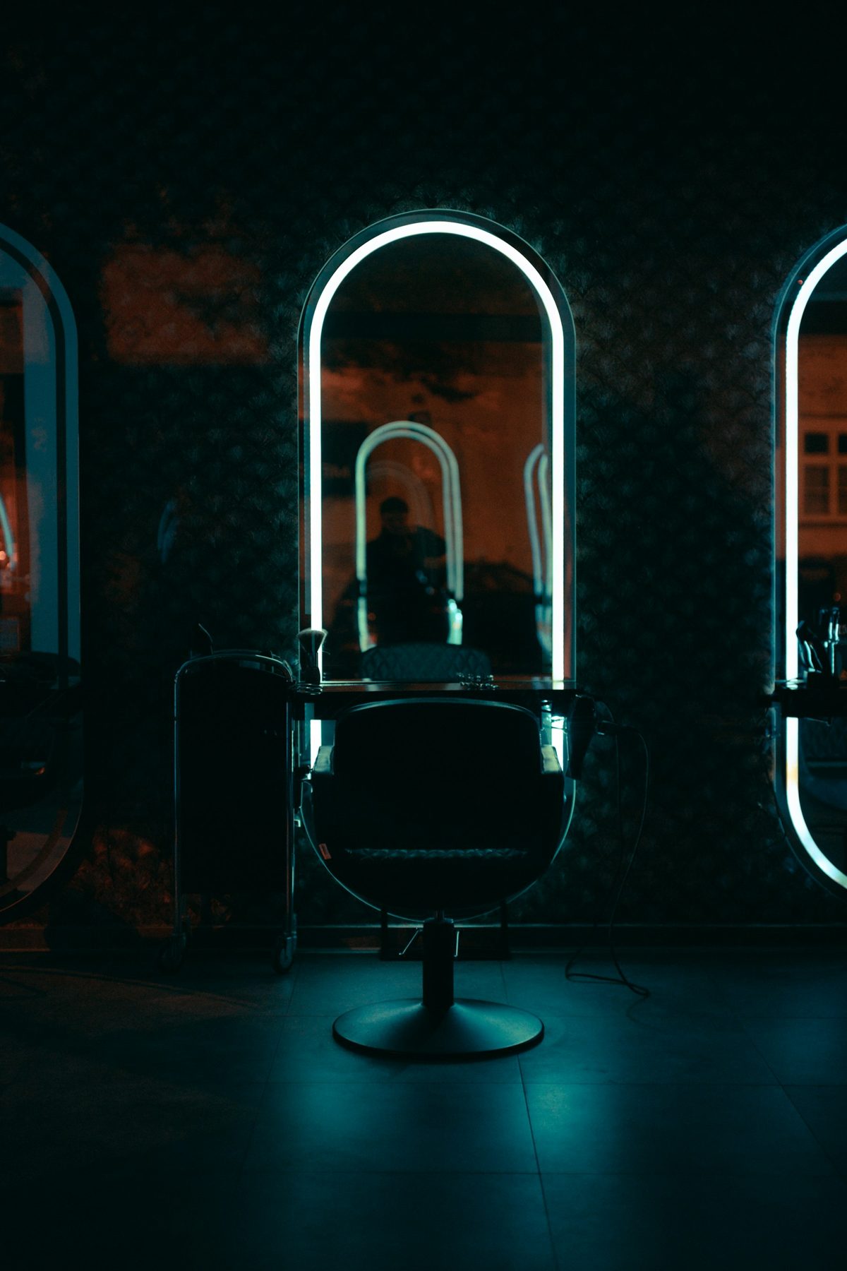 A salon chair in front of an arched mirror with glowing white neon lighting