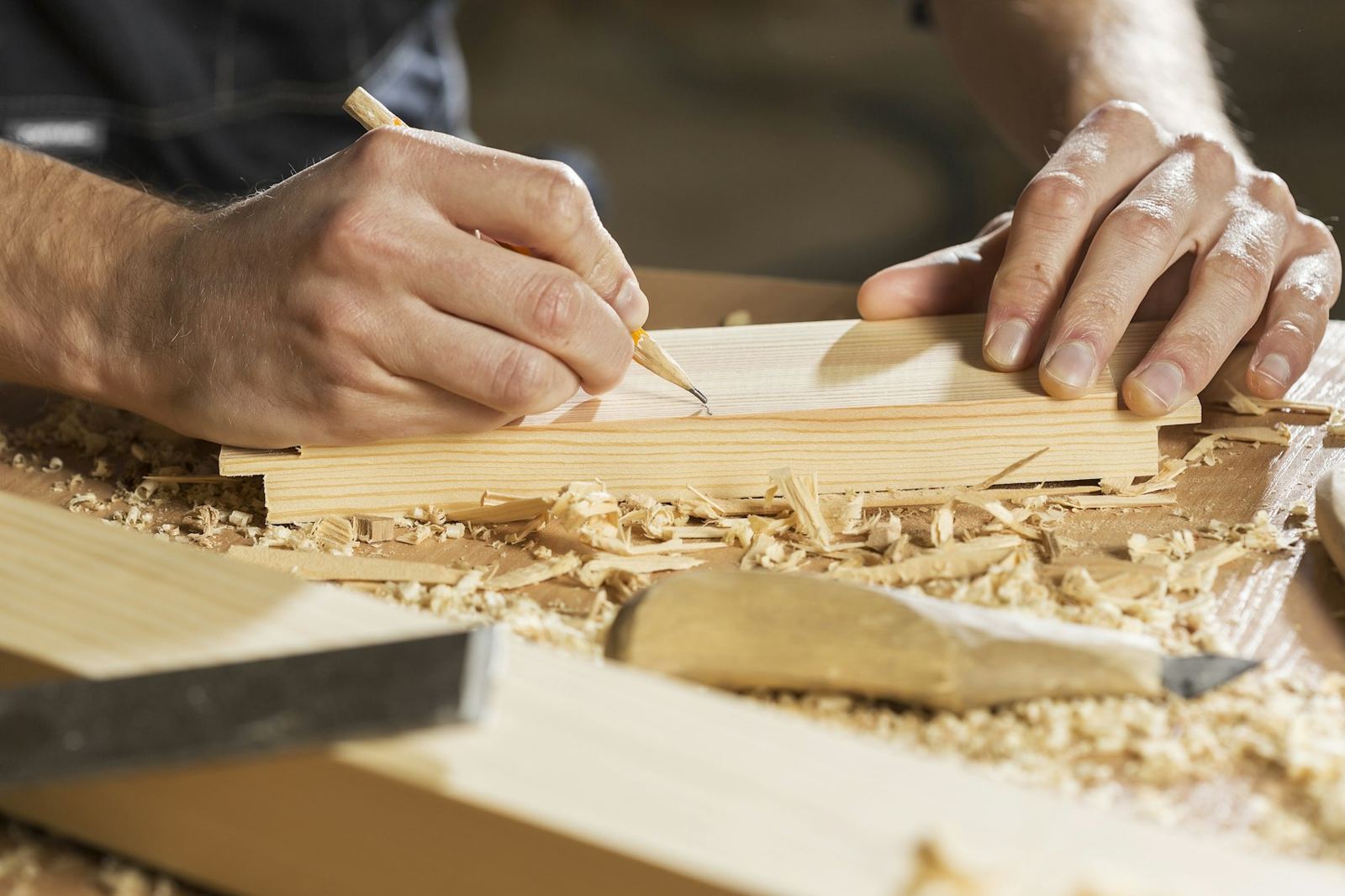 Carpenter marking a board with a pencil among wood shavings