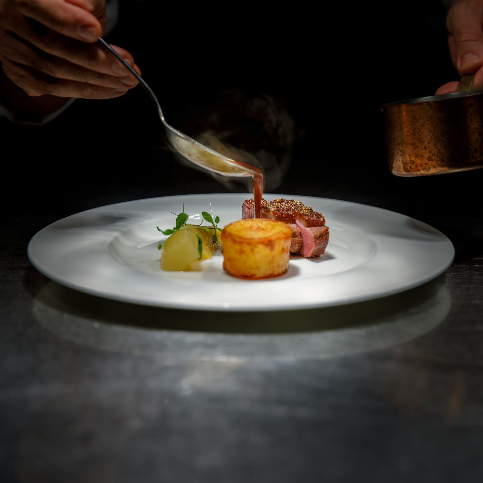 A plate being finished with sauce in a dark kitchen