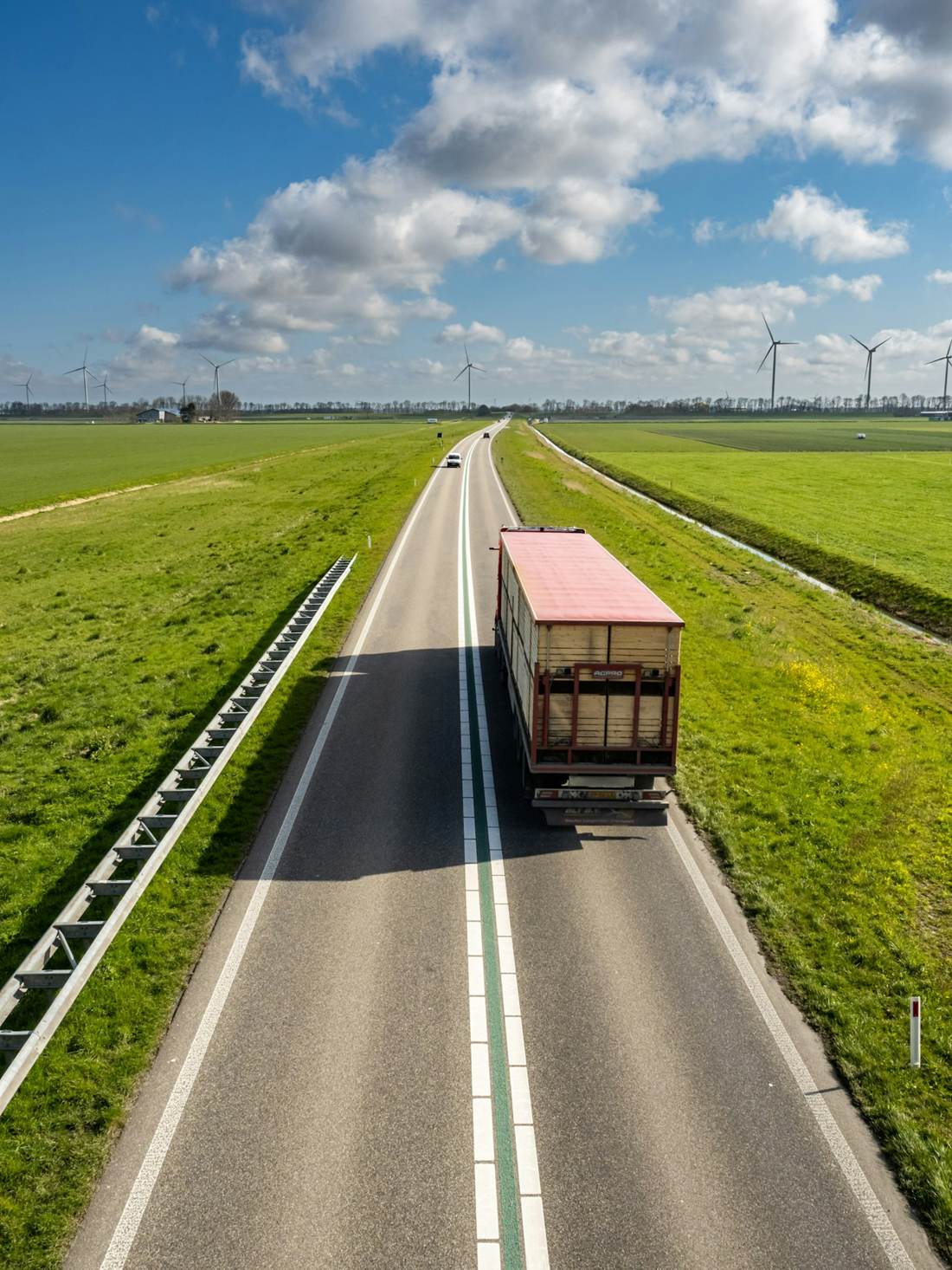 Truck on a long straight road through green fields