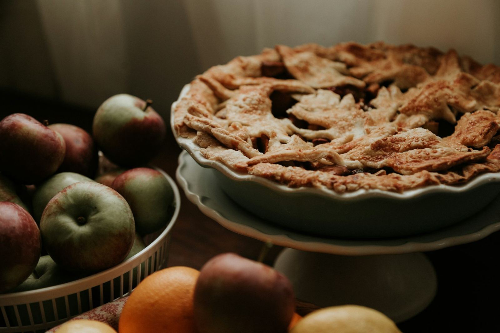 Lattice pie on a cake stand beside a bowl of apples