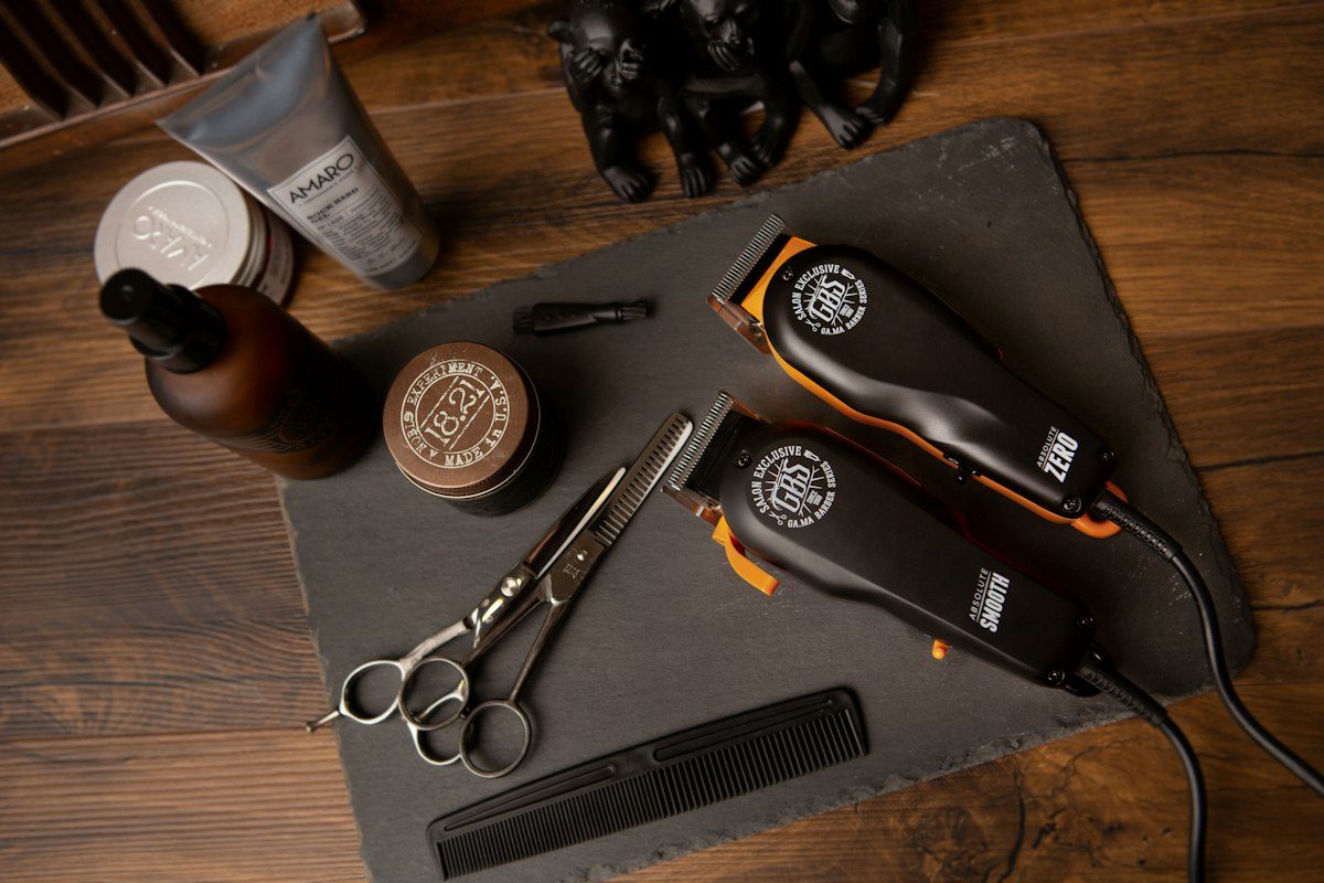Two hair clippers, scissors, a comb, and grooming products on a slate board