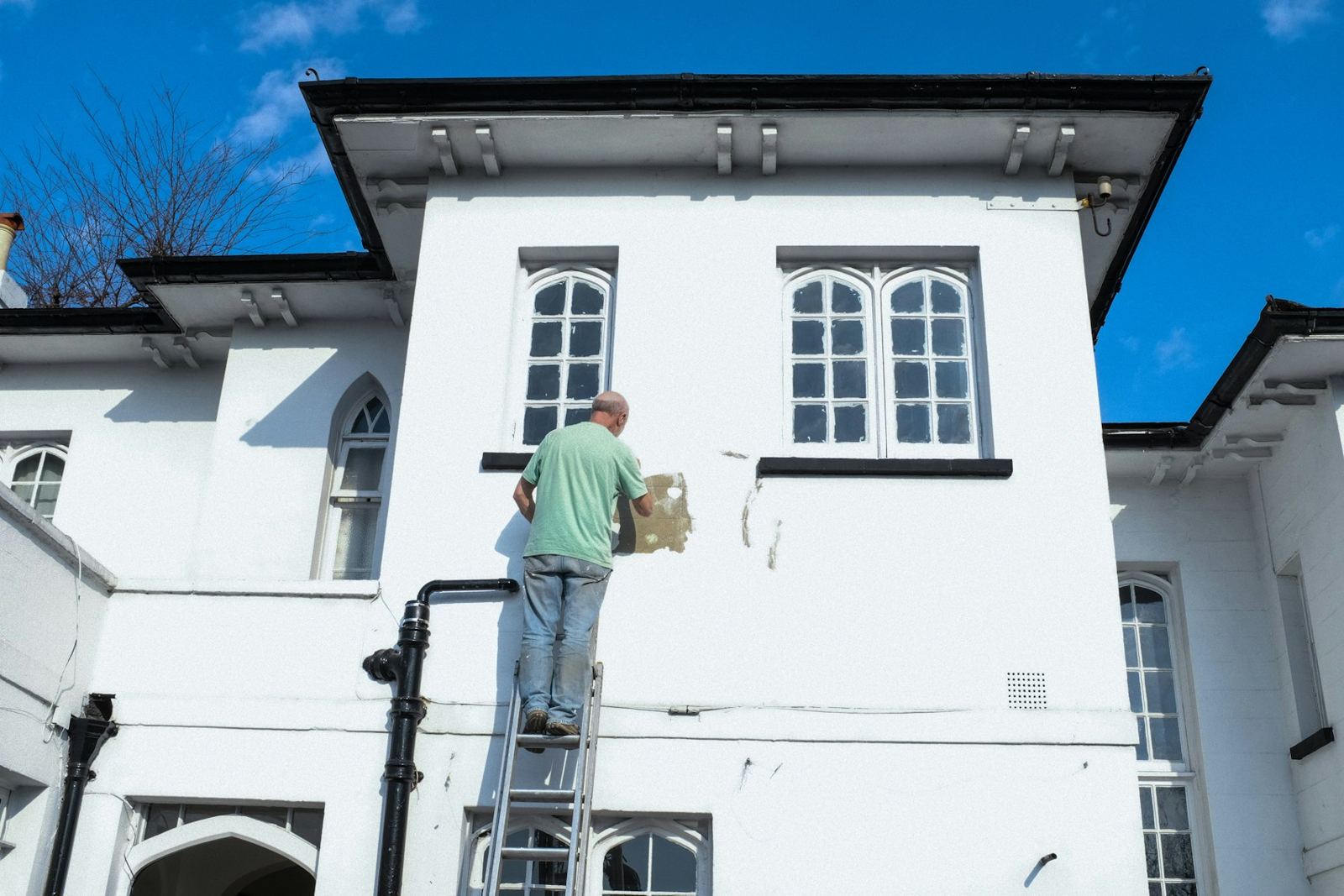 Painter on a ladder at a white building with dark trim