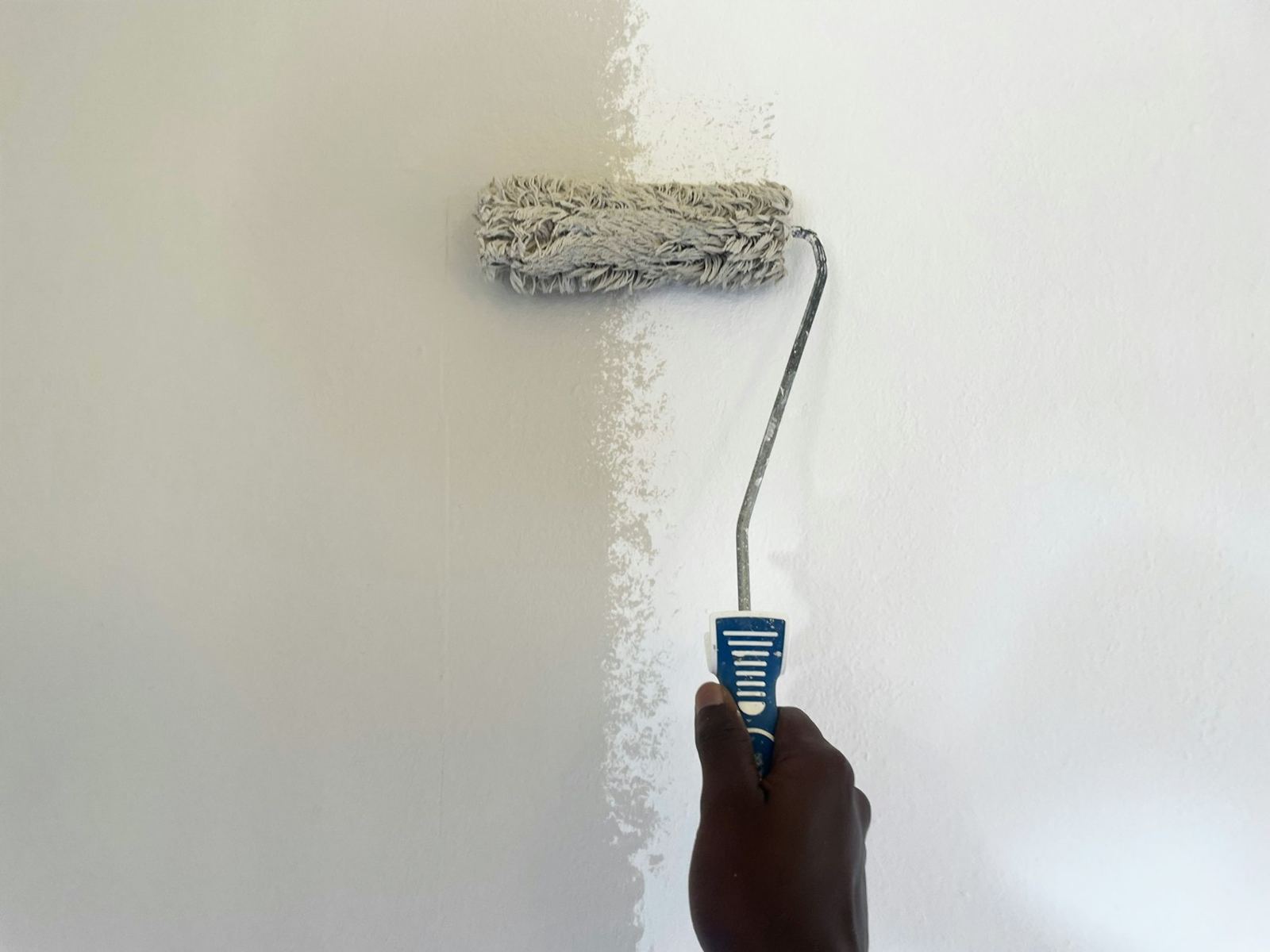 Hand using a paint roller on a pale wall