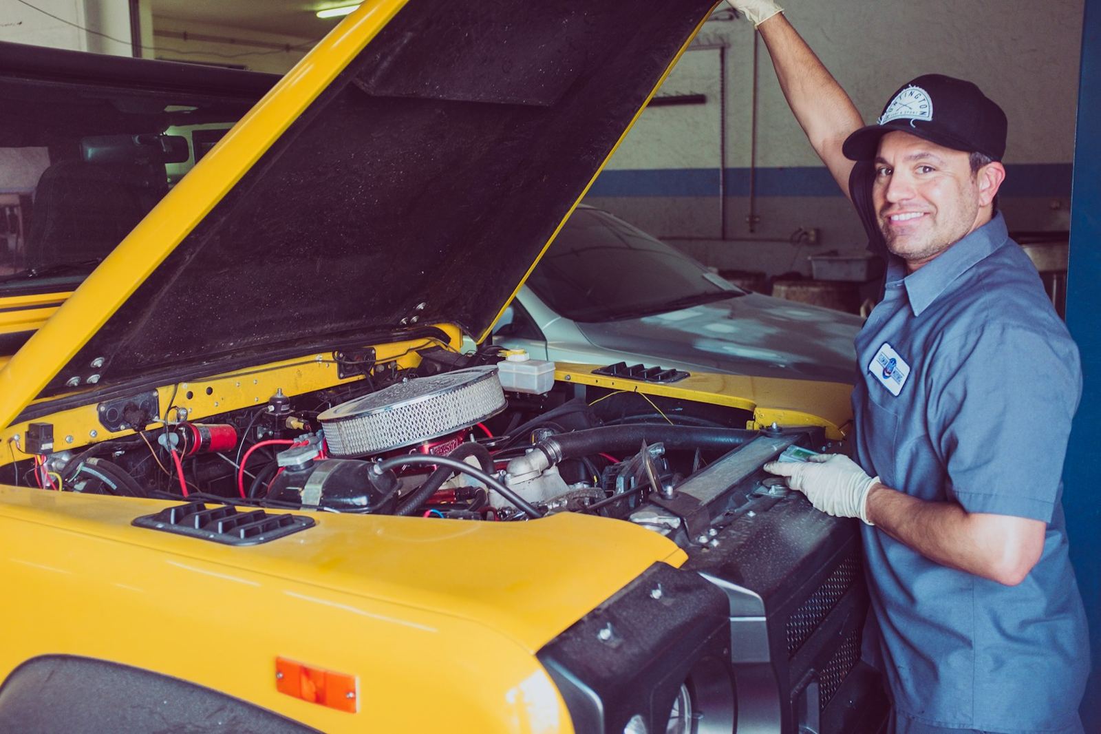 Smiling mechanic working under the hood of a yellow car
