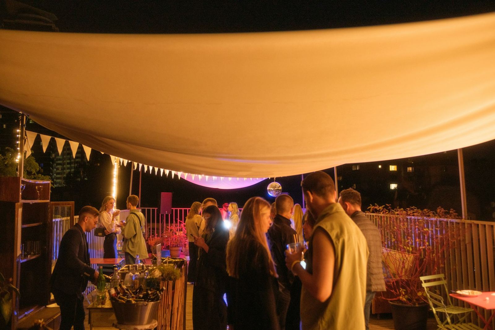 Guests gathered under a canopy on a rooftop terrace in the evening
