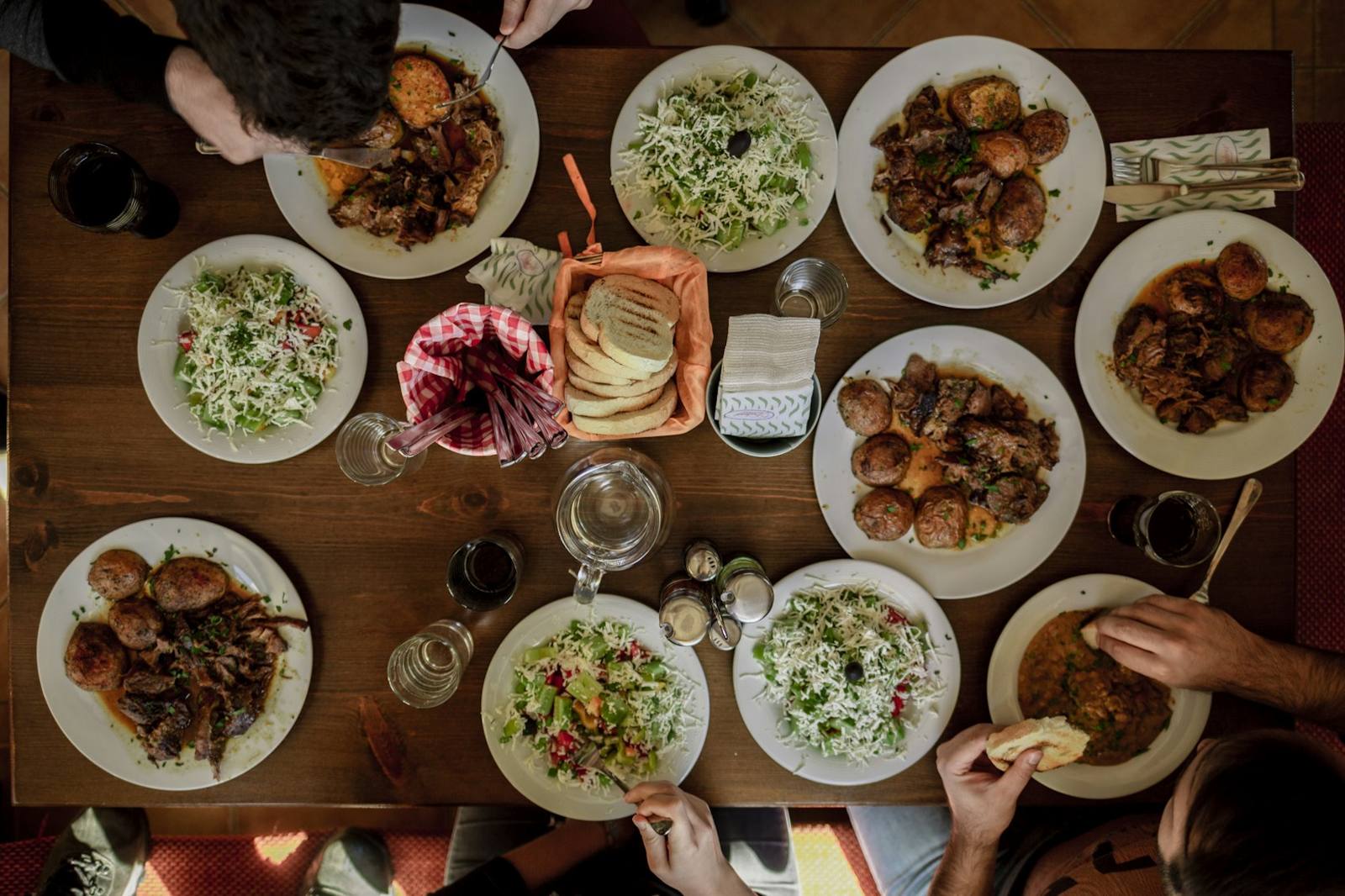 Hands reaching across a table full of shared plates from above