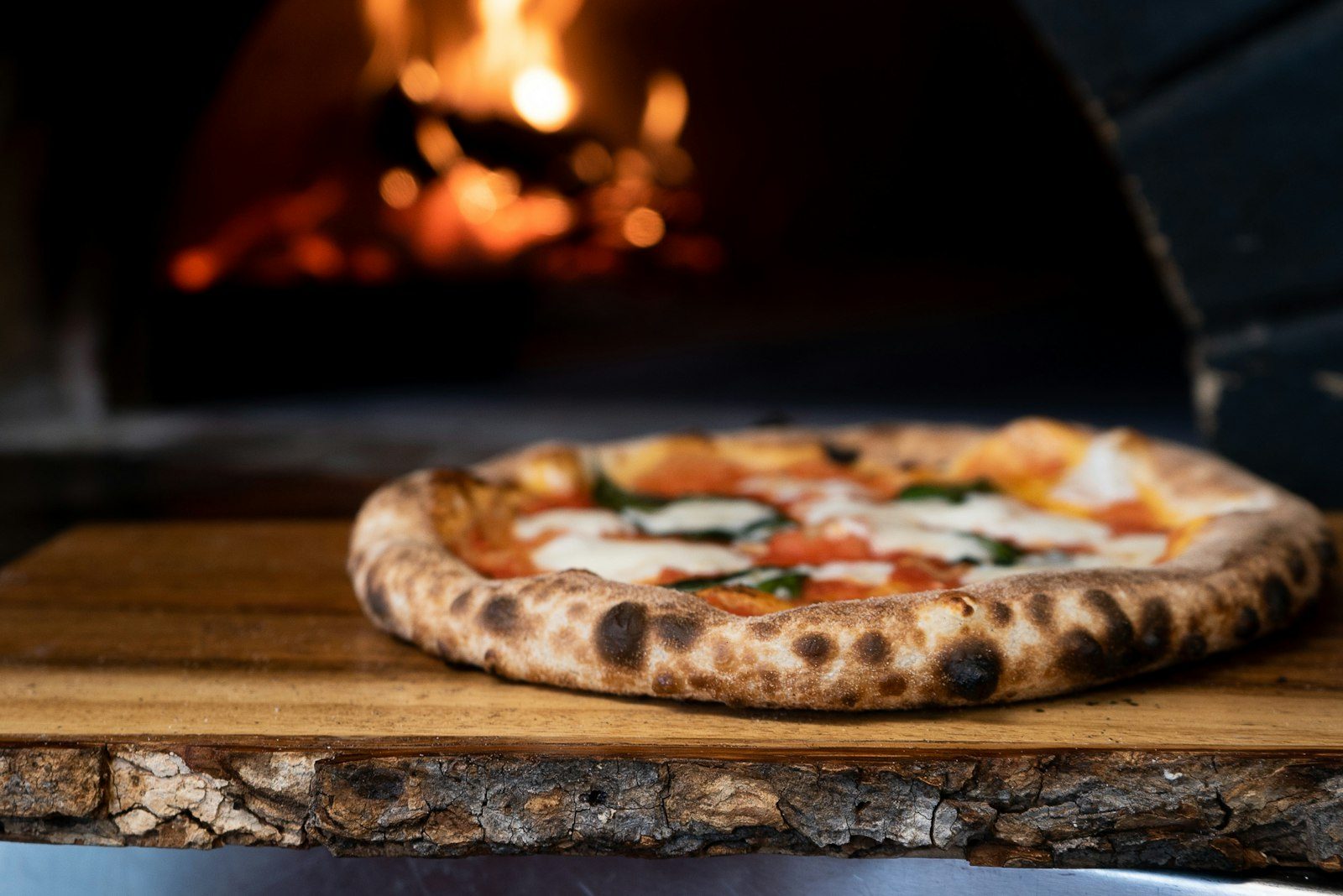 A blistered pizza in front of a wood-fired oven