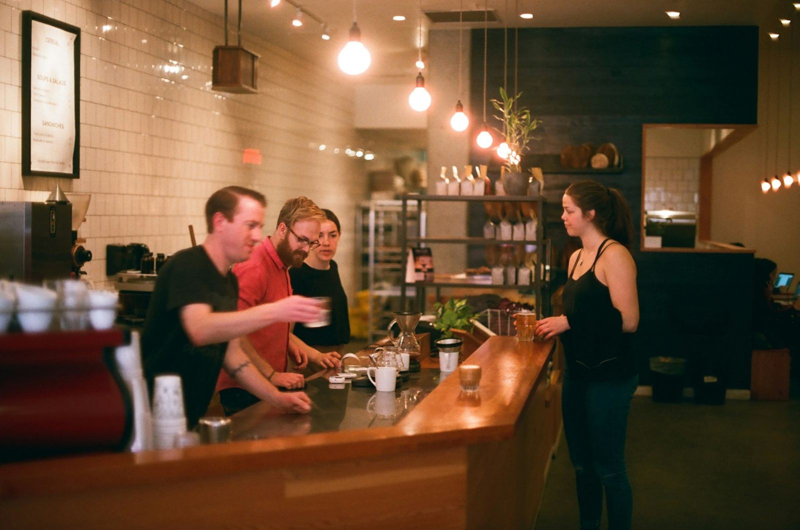 Friends chatting at a wooden coffee bar under warm lights